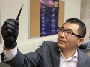 A man holds up a tiny chip in a university lab.