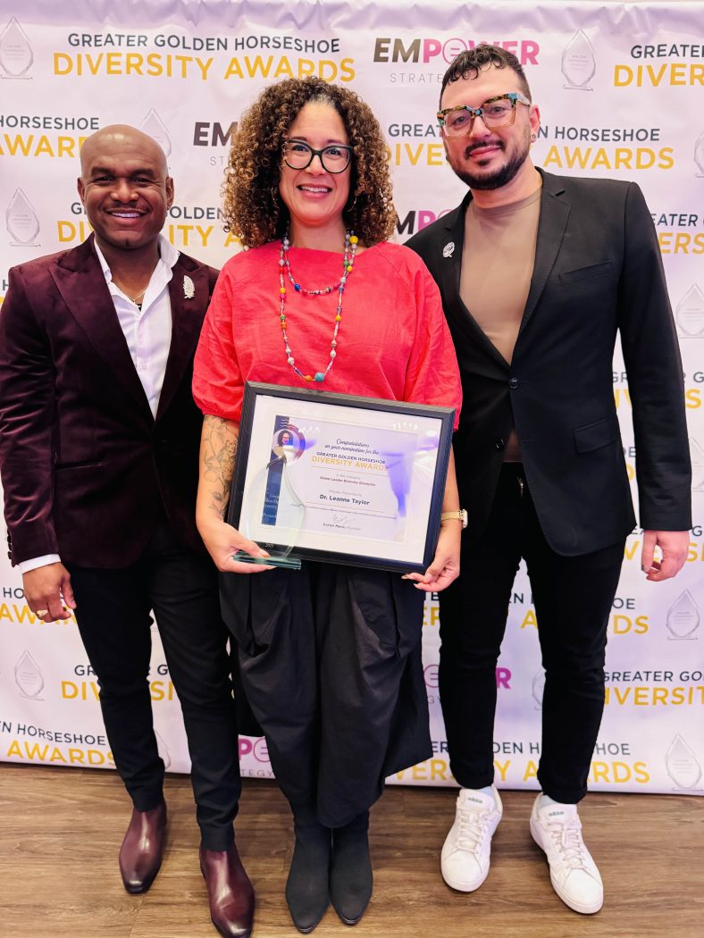Three people stand together, one holding an award.