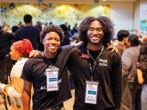 Two young men pose side-by-side in a university cafeteria.