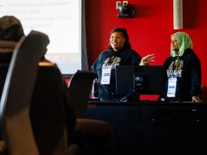 Two women talk to high school students from the front of a classroom.