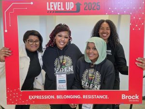 Four black women stand side-by-side with a large, paper picture frame.