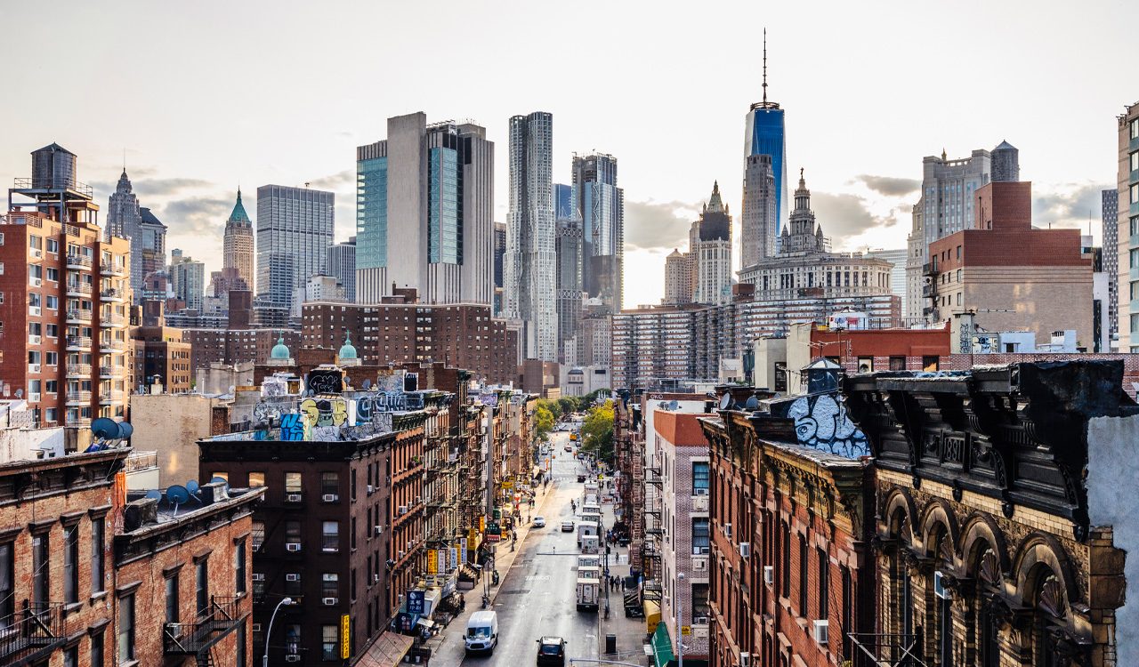 Aerial view of New York City neighbourhood with brown buildings, skyscrapers and cars on the road.