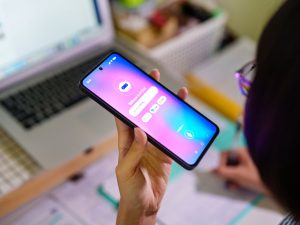 Person holds a cell phone using AI while working on a computer.