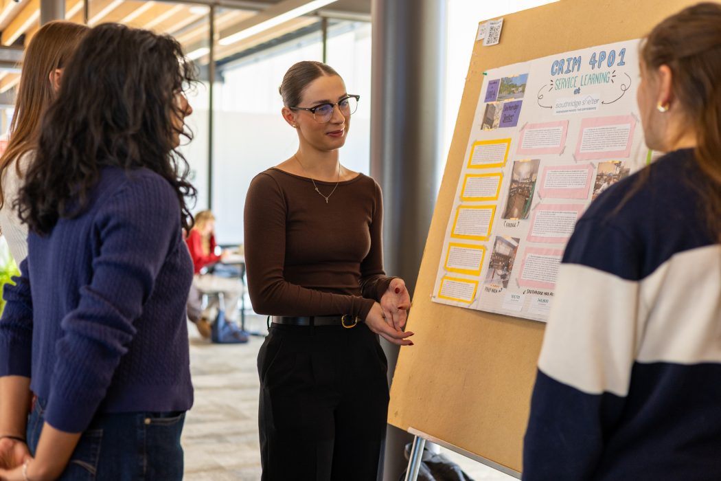 A woman speaks to three other women while they stand around a poster board.