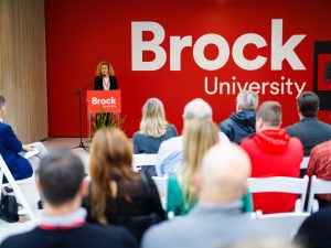 A woman stands at a podium speaking to a crowd.
