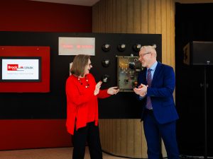 Two people smile and gesture toward each other while unveiling or demonstrating a Brock SPARK display panel.