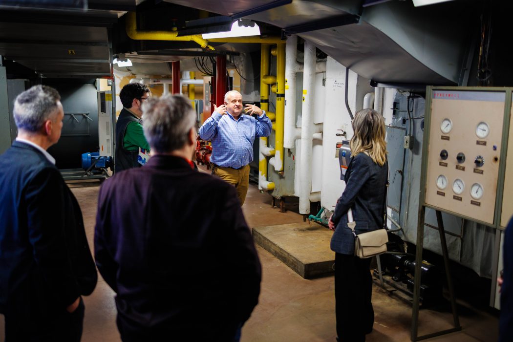 A staff member leads a small group on a tour inside a mechanical room, explaining the facility’s equipment.