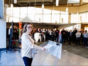 Lesley Rigg smiling at a podium while presenting to a group of Brock faculty and staff gathered in a large brightly lit room an awards celebration.