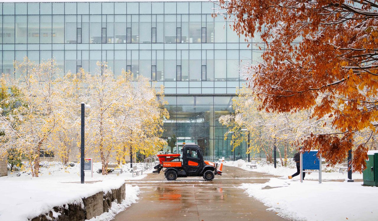 A small vehicle drives through a snowy university campus