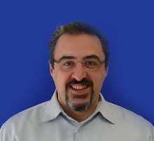 A man is shown from the shoulders up smiling against a blue background.