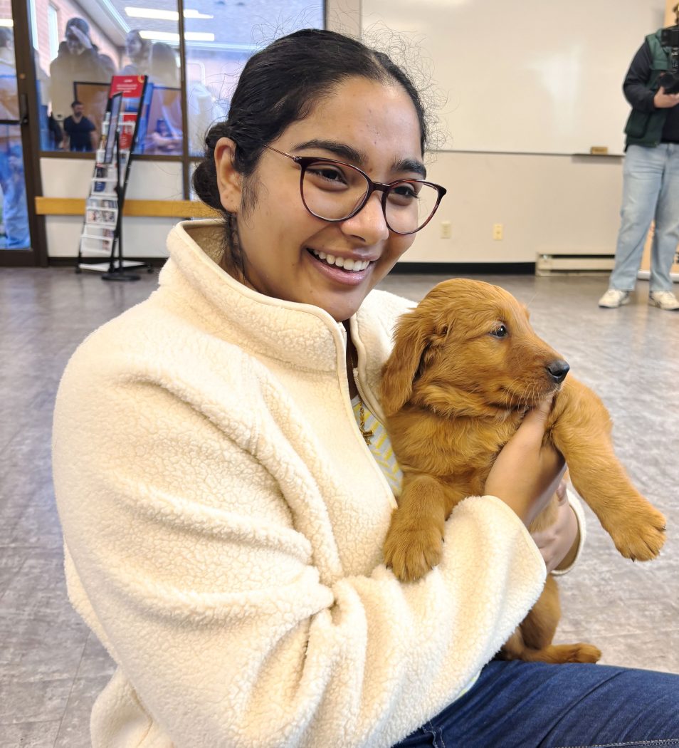 A woman smiles while holding a small puppy.