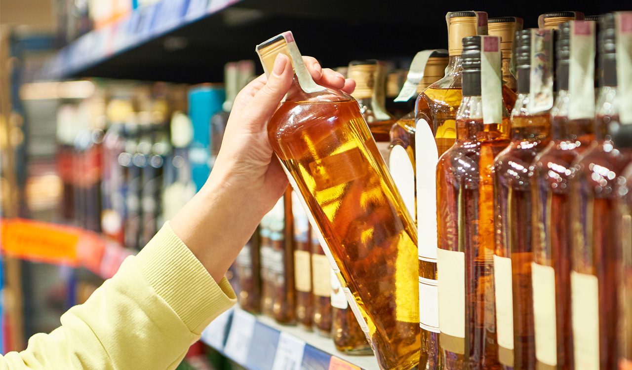 Person pulls a liquor bottle from a store shelf.