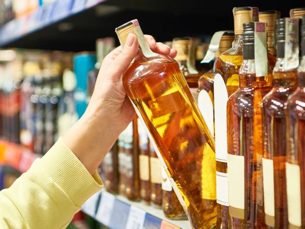 Person pulls a liquor bottle from a store shelf.