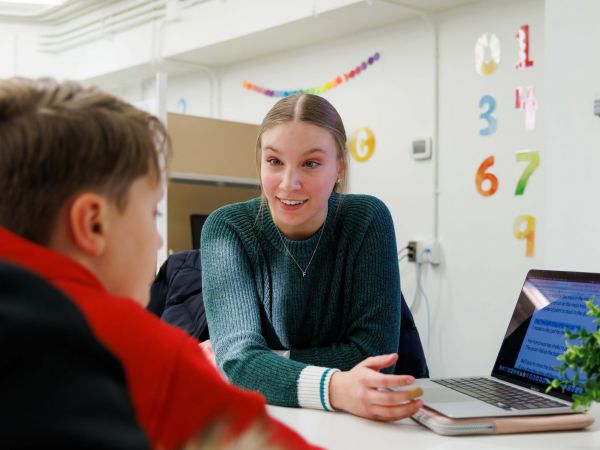 A woman sits across a desk from a child while teaching.