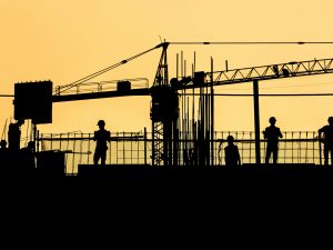 A silhouette of people working on a construction site with a crane and fencing.