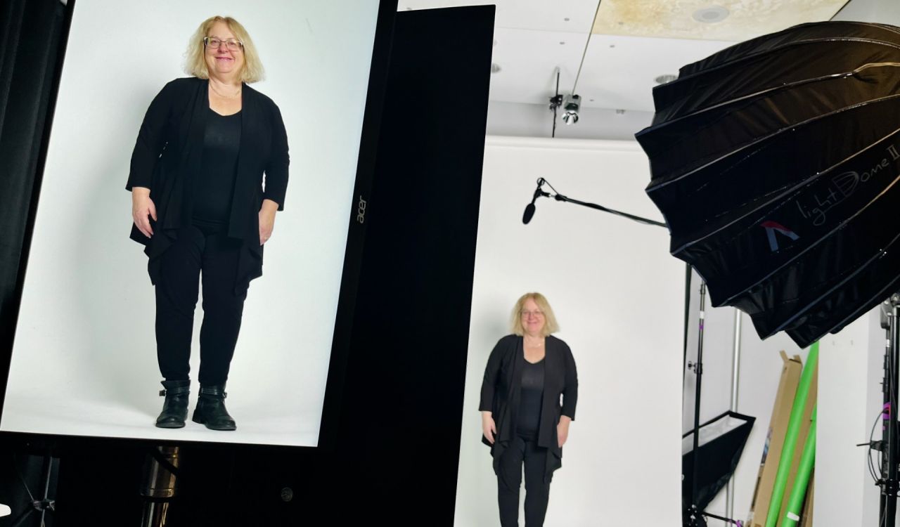 A screen displays the image of Francine McCarthy as she stands in the distance against a white backdrop, with a microphone and a hooded light stand pointing at her.