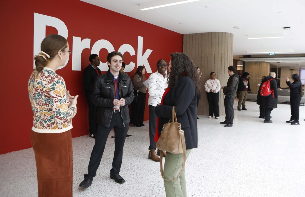Several groups of people chat in front of a red wall at an event.