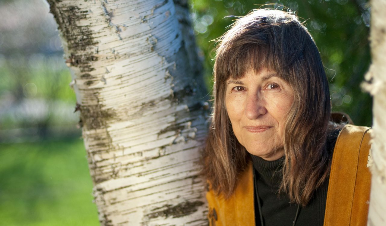 A woman stands beside a birch tree.