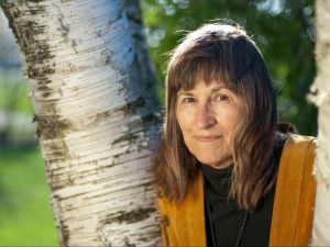 A woman stands beside a birch tree.