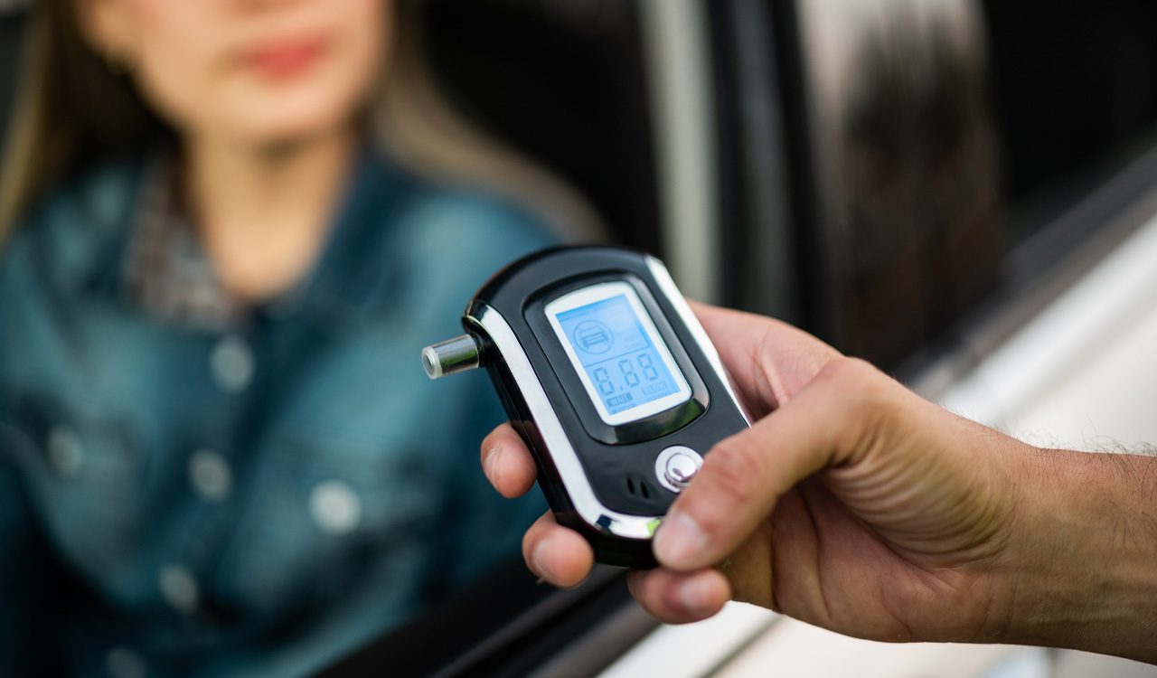 Someone holds breathalyzer in front of woman in a car.