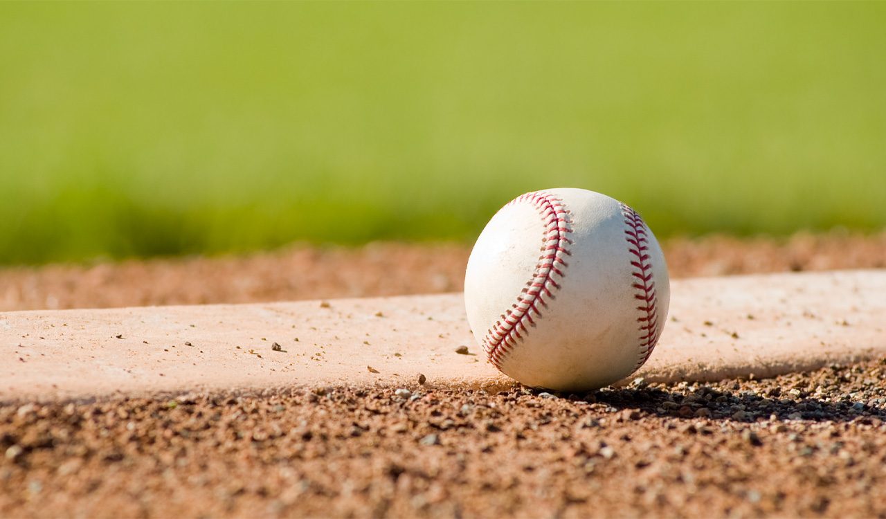Baseball rests on a pitching mound on a baseball diamond.