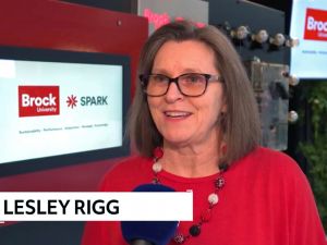 Woman does a television interview in front of a screen that says Brock University and spark.