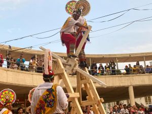 A group of circus artists in colourful costumes perform in an amphitheater doing acrobatics on tall wood structures.