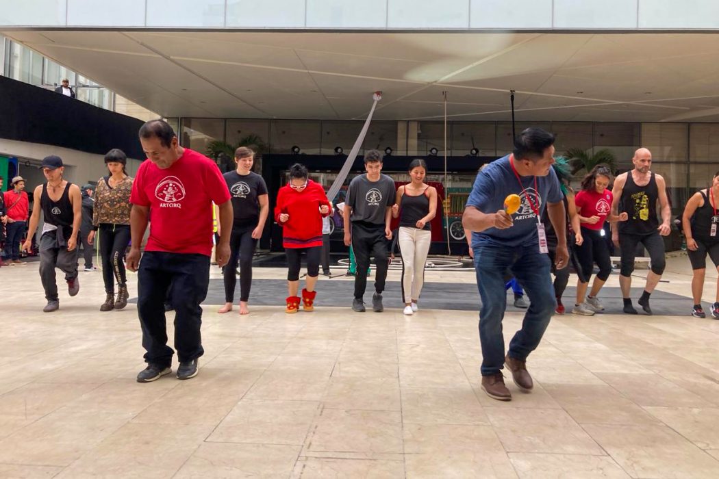 A group of people dance together outside in front of a building. 