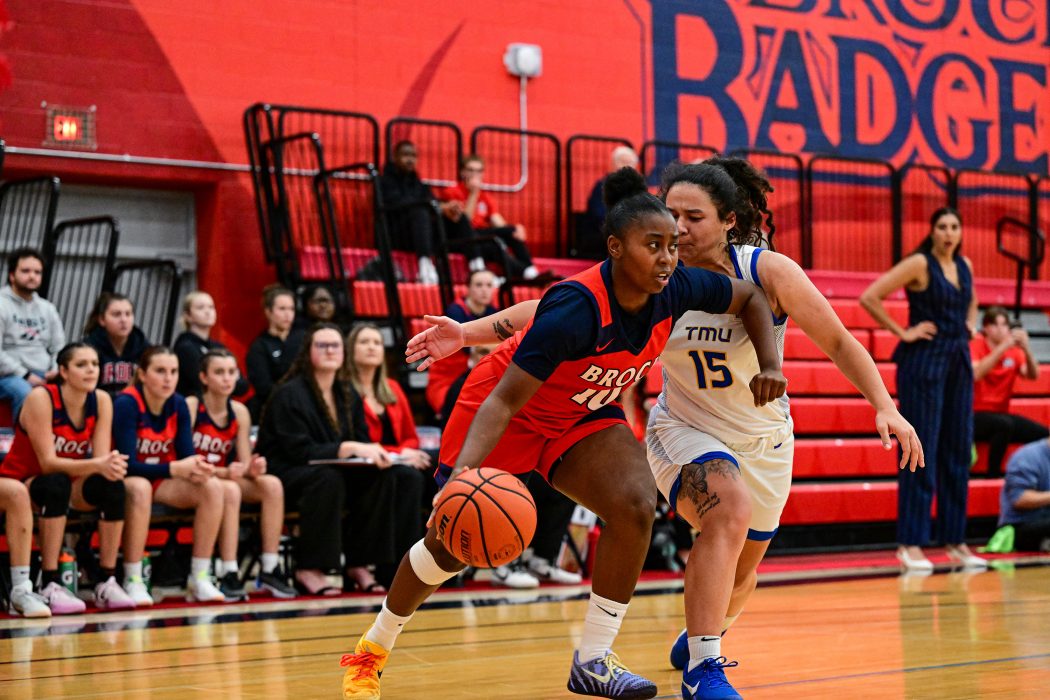 Two women play basketball during a game in a university gymnasium.