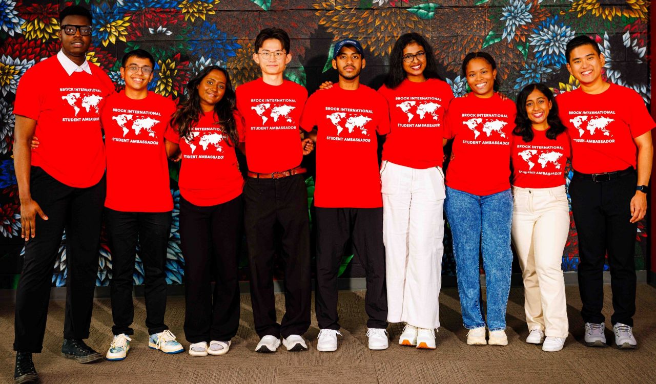 A group of university students in red t-shirts pose for a photo in front of a flower mural.