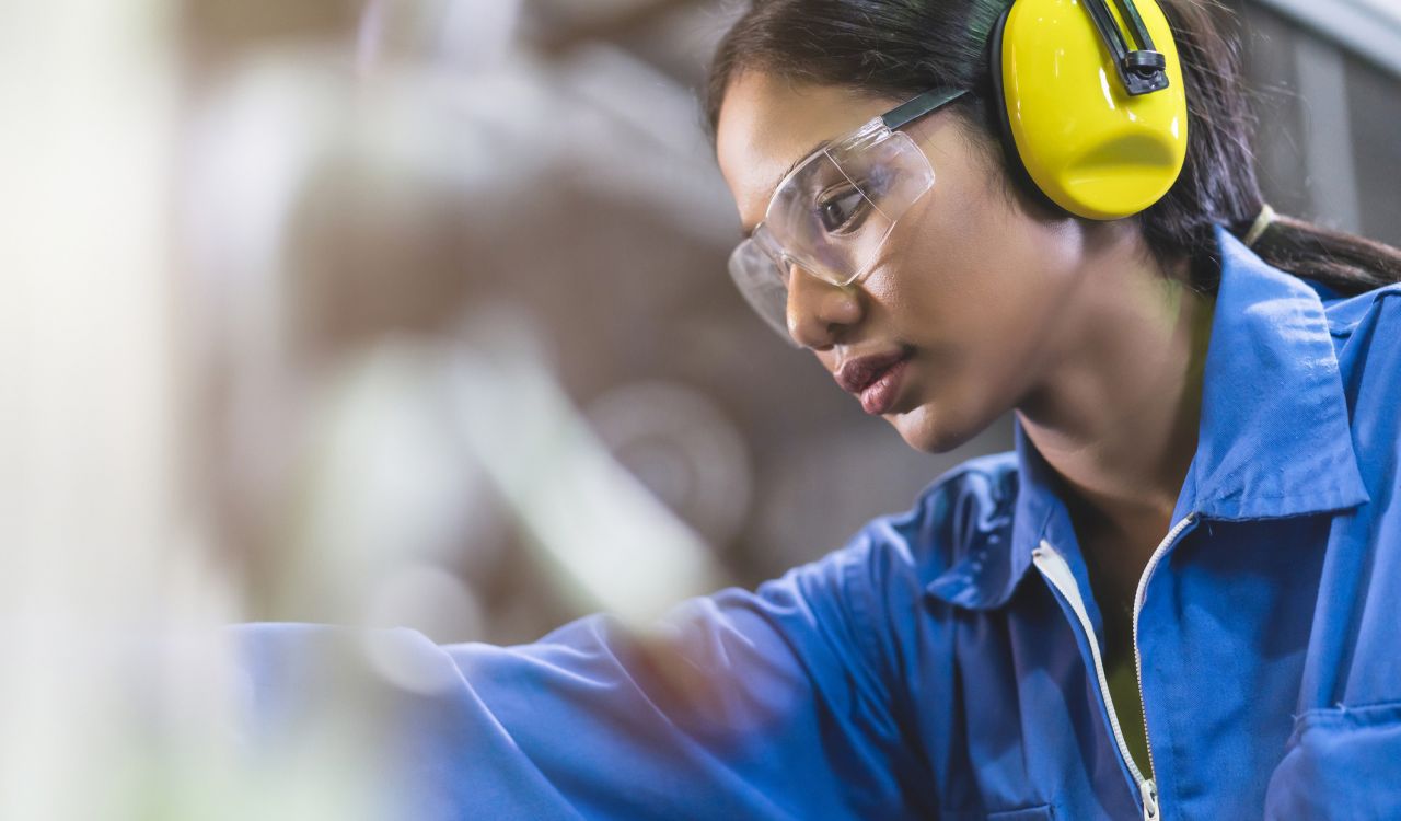 A woman wearing safety gear works in a skilled trade.