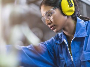 A woman wearing safety gear works in a skilled trade.