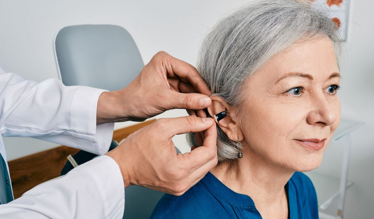 A health-care professional helps an older woman put in a hearing aid.