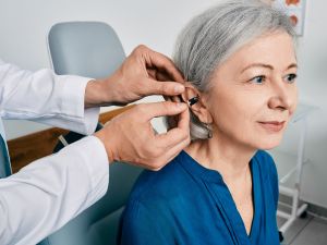 A health-care professional helps an older woman put in a hearing aid.