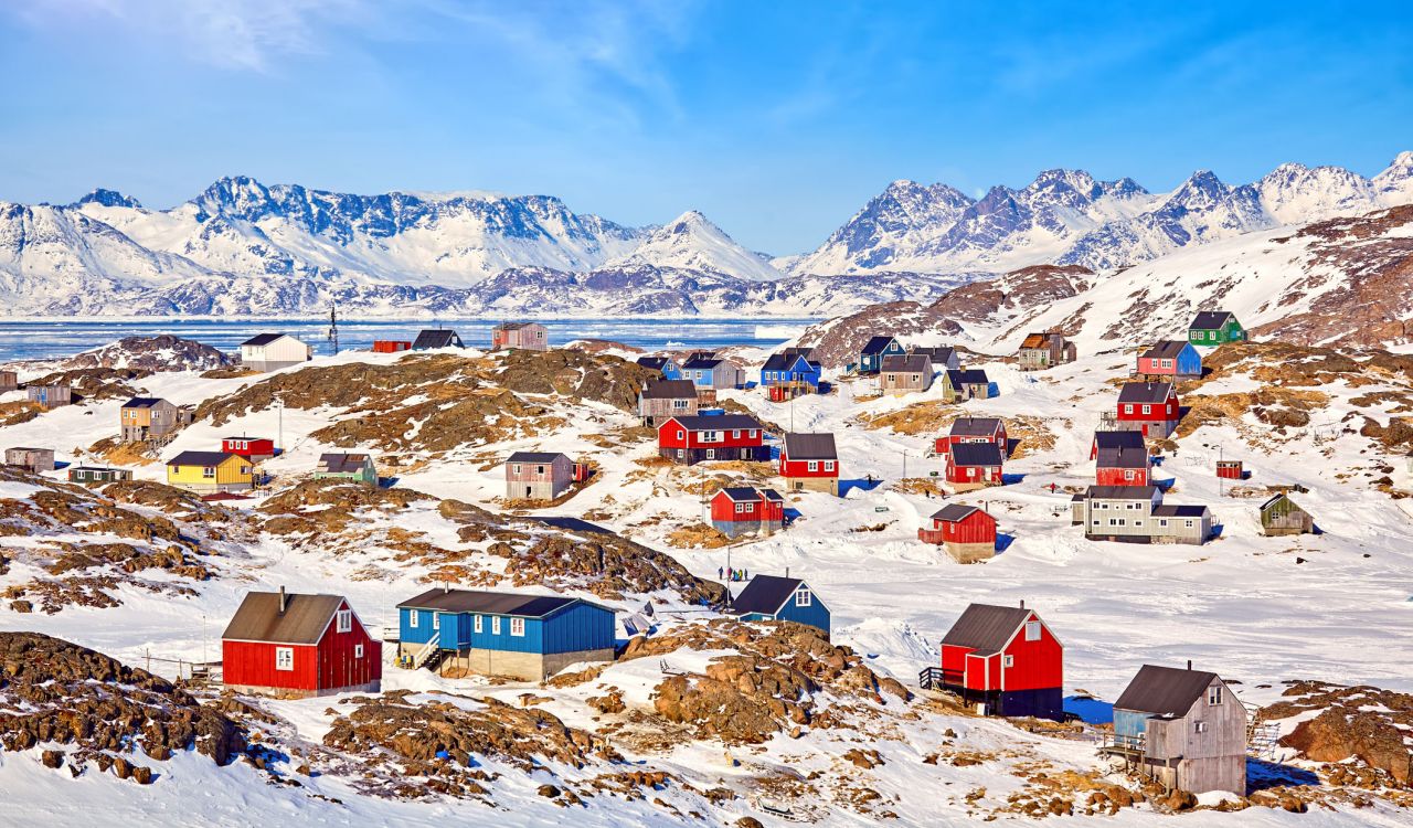Colourful homes dot snowy hills in a Greenland village, with snow-capped mountains in the distance.