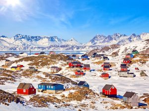 Colourful homes dot snowy hills in a Greenland village, with snow-capped mountains in the distance.