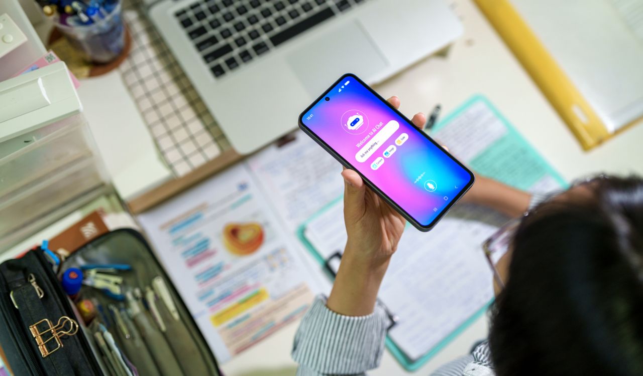 Close-up of an AI chatbot on the screen of a mobile phone being held by a person sitting at a desk.