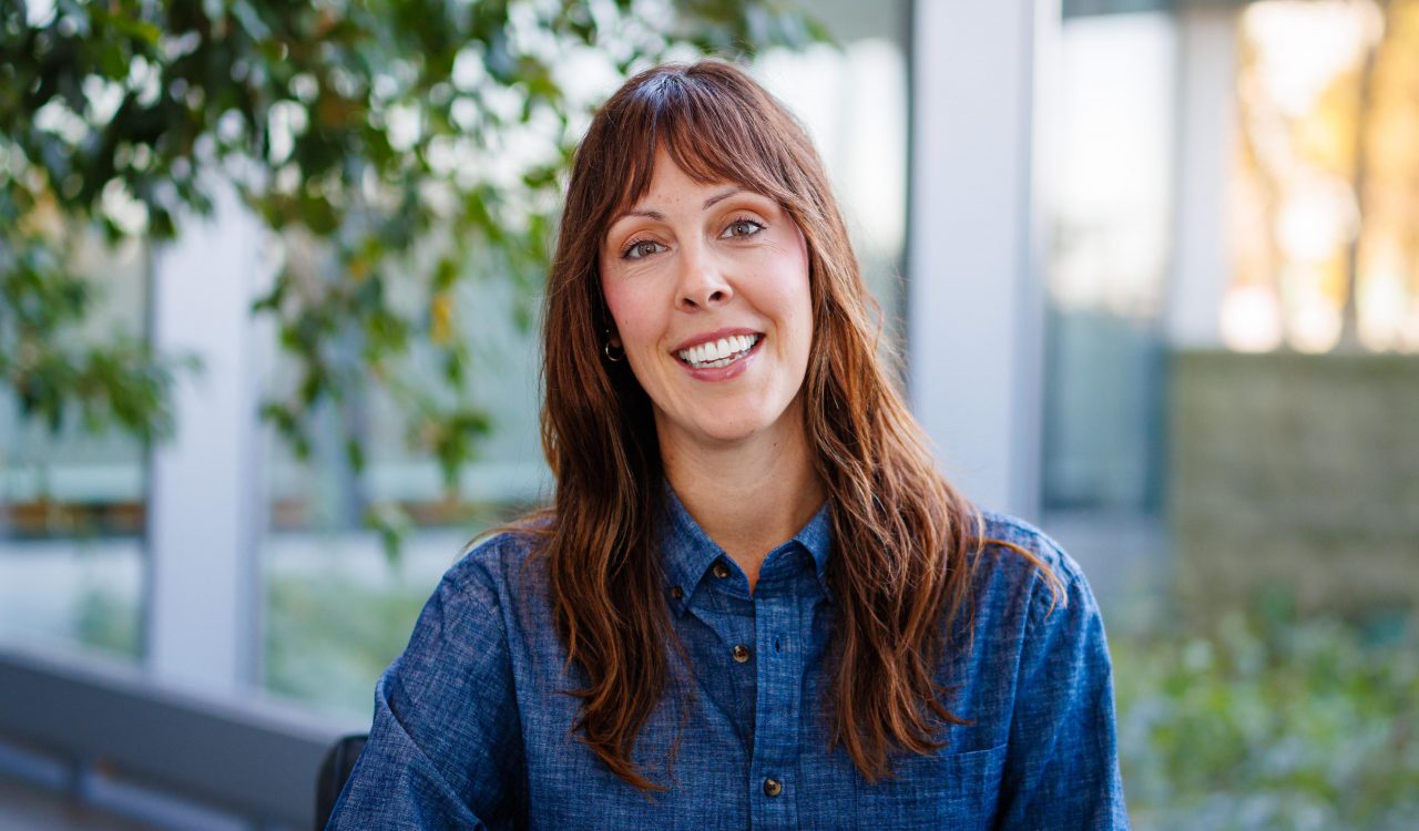 Portrait of a woman with a window and green space behind her.