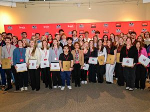 A group of people holding certificates pose for a photo in front of a red backdrop.