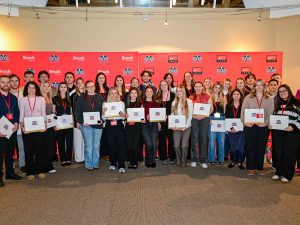 A group of people holding certificates pose for a photo in front of a red backdrop.