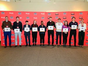 A group of people holding certificates pose for a photo in front of a red backdrop.