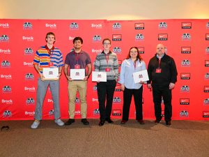 A group of people holding certificates pose for a photo in front of a red backdrop.