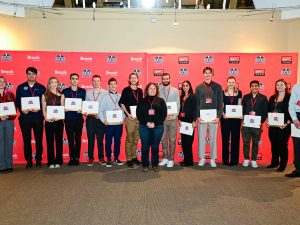 A group of people holding certificates pose for a photo in front of a red backdrop.