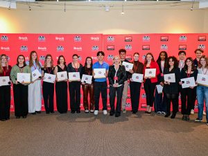A group of people holding certificates pose for a photo in front of a red backdrop.