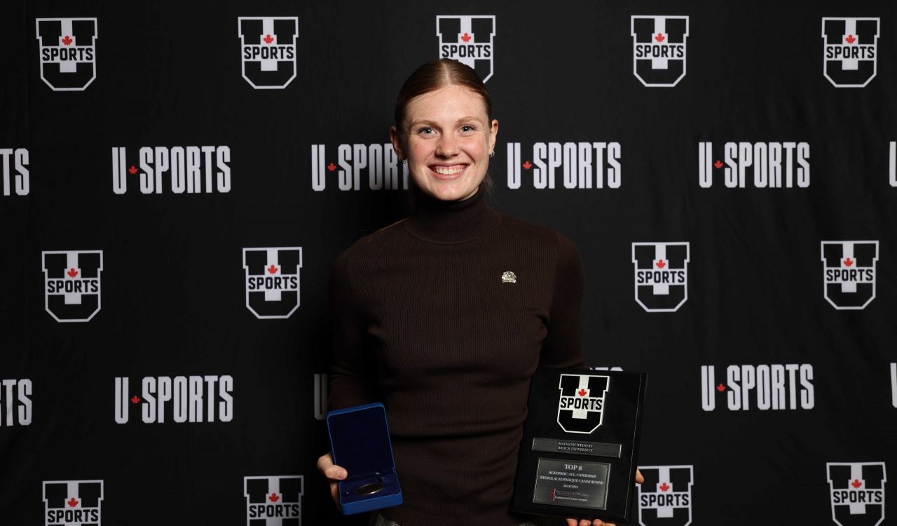 A young woman poses in front of a black backdrop holding two awards.