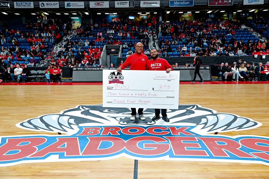 Two people stand on a basketball court holding a large cheque.