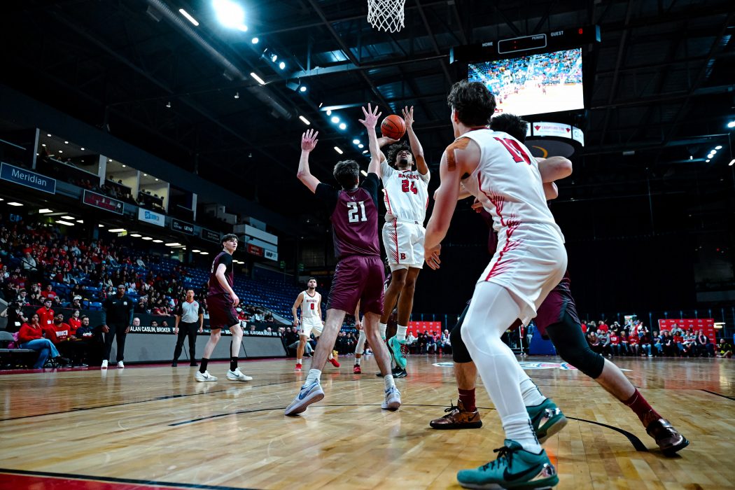 A man drives a basketball towards the hoop while he's guarded on a large arena court.