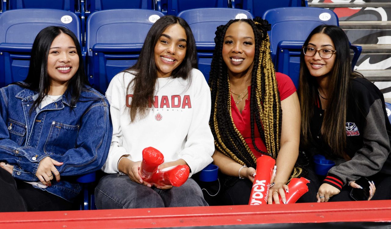 Four university students sit beside each other while watching a basketball game.