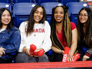 Four university students sit beside each other while watching a basketball game.