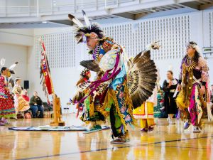 A person in Indigenous regalia dances in a gymnasium.